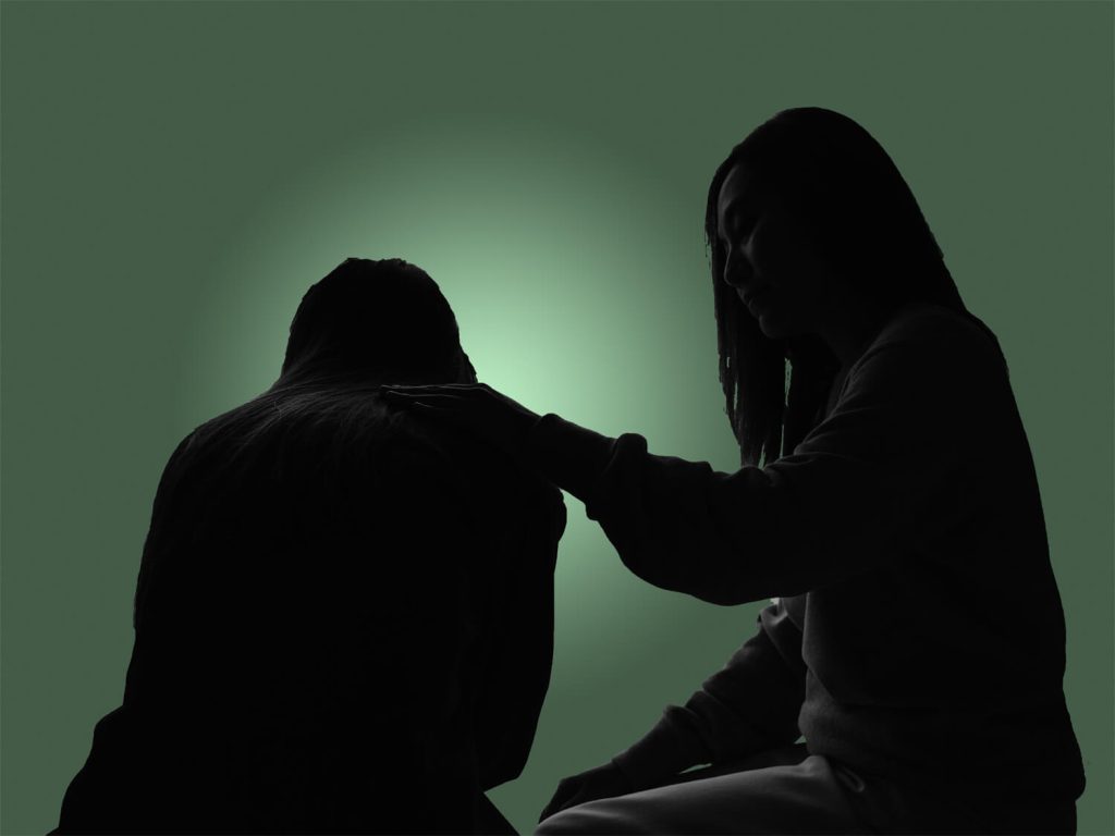 A woman kneeling to assist a man, depicted in silhouette against a light background