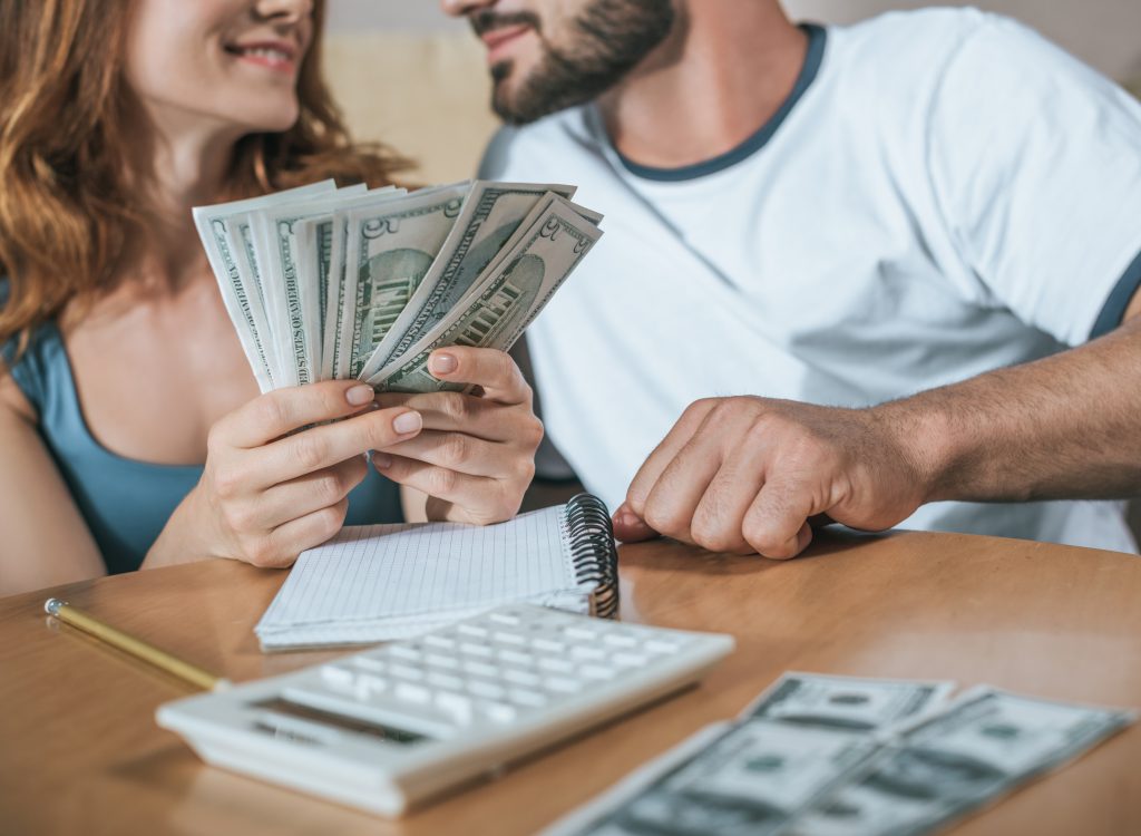 cropped image of couple planning family budget and holding dollars in living room
